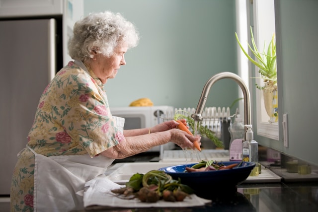 A woman in a floral dress washing carrots, representing healthy eating and quality of life for the elderly, the theme of the Solidarity Supplement for the Elderly.